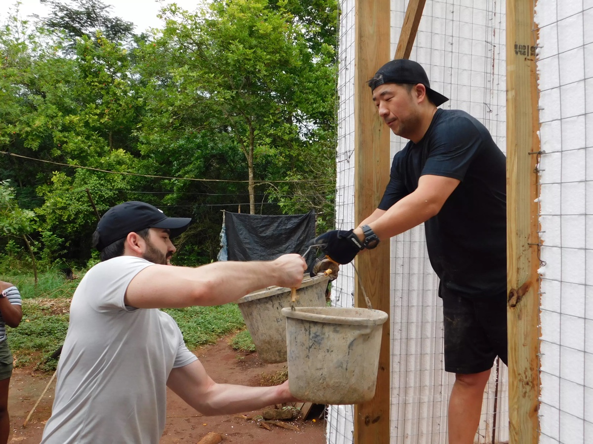 Two men passing a bucket of cement in a home under construction
