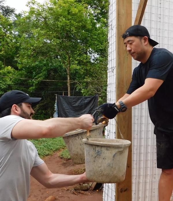 Two men passing a bucket of cement in a home under construction