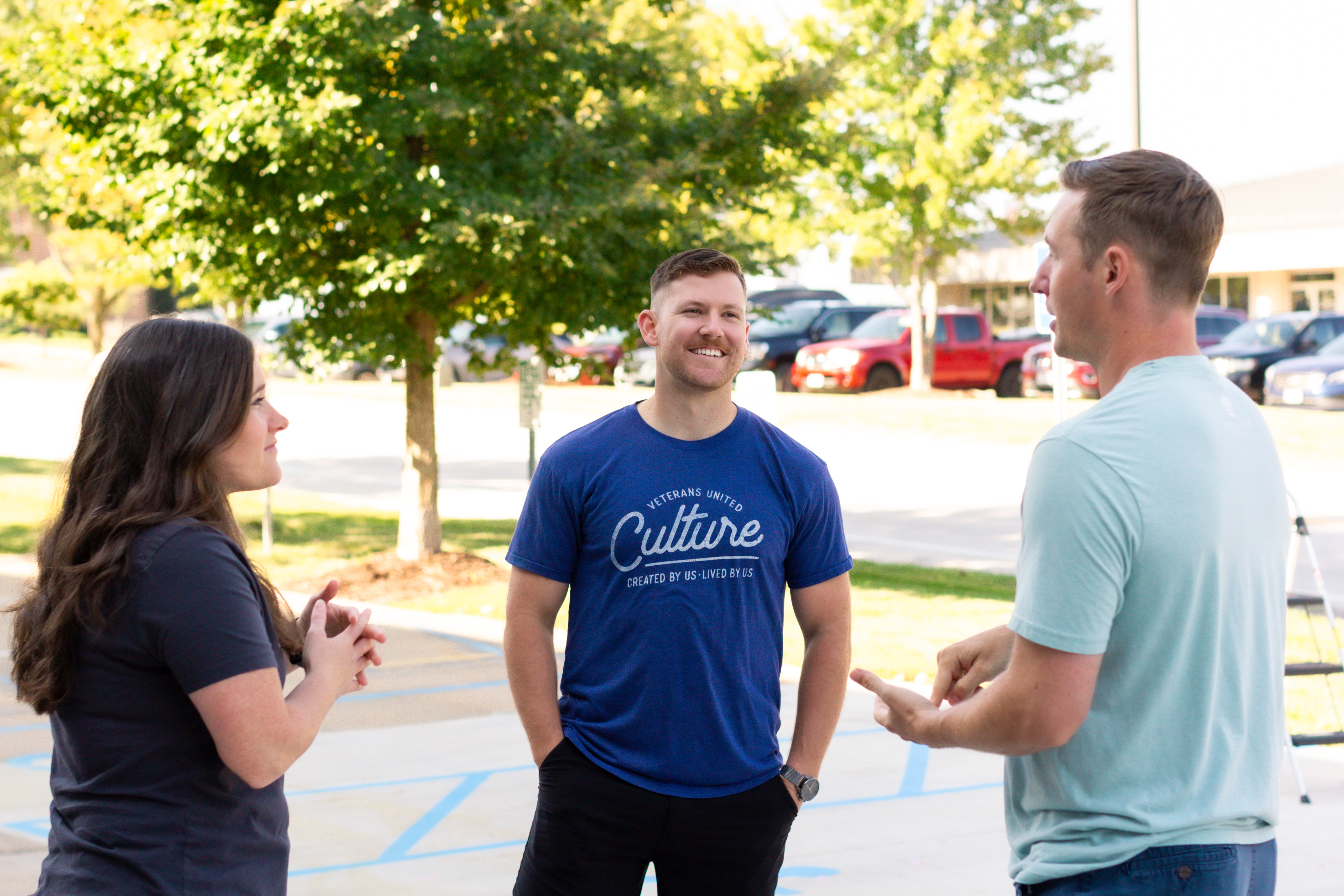 1 female and 2 male employees smiling and talking outside on a sunny day