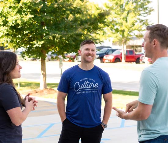 1 female and 2 male employees smiling and talking outside on a sunny day