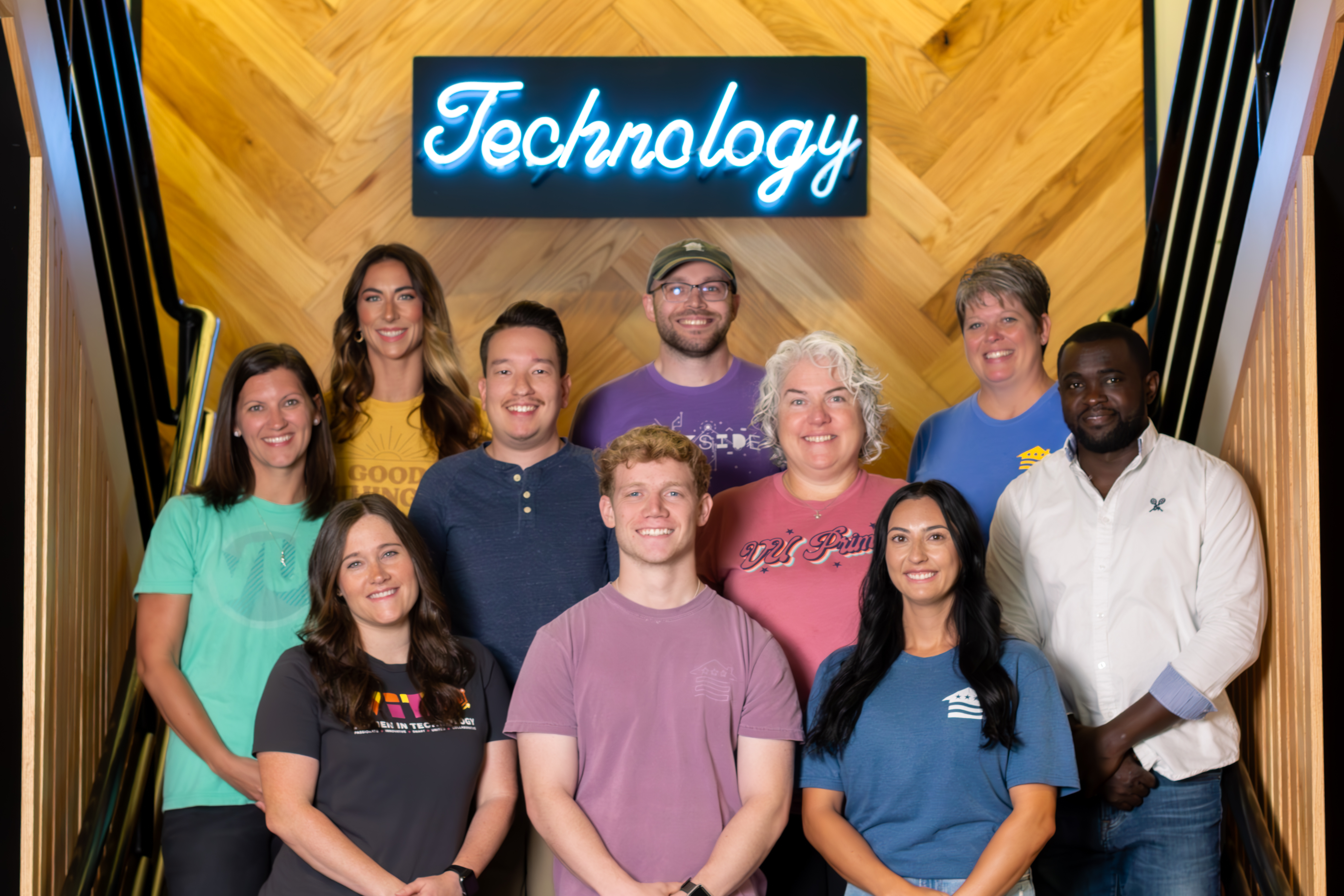 10 employees standing on stairs smiling with neon blue technology sign behind them