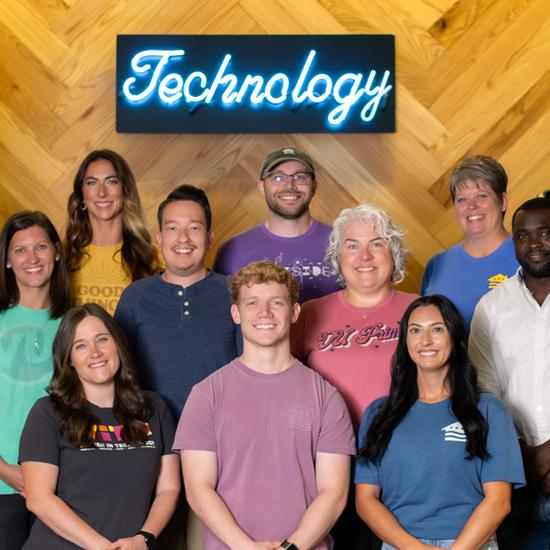 10 employees standing on stairs smiling with neon blue technology sign behind them