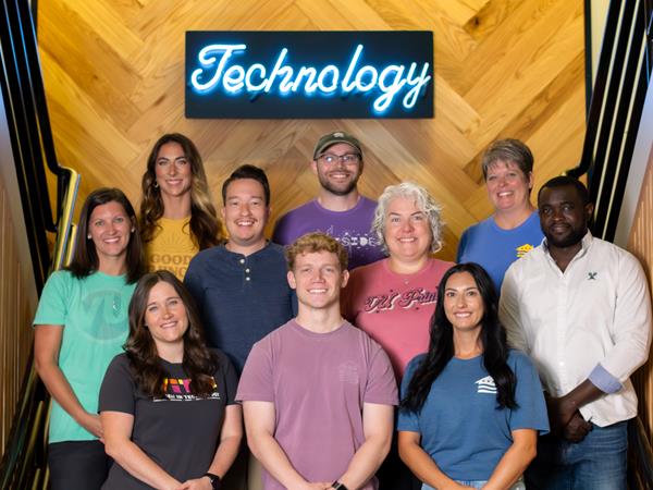 10 employees standing on stairs smiling with neon blue technology sign behind them