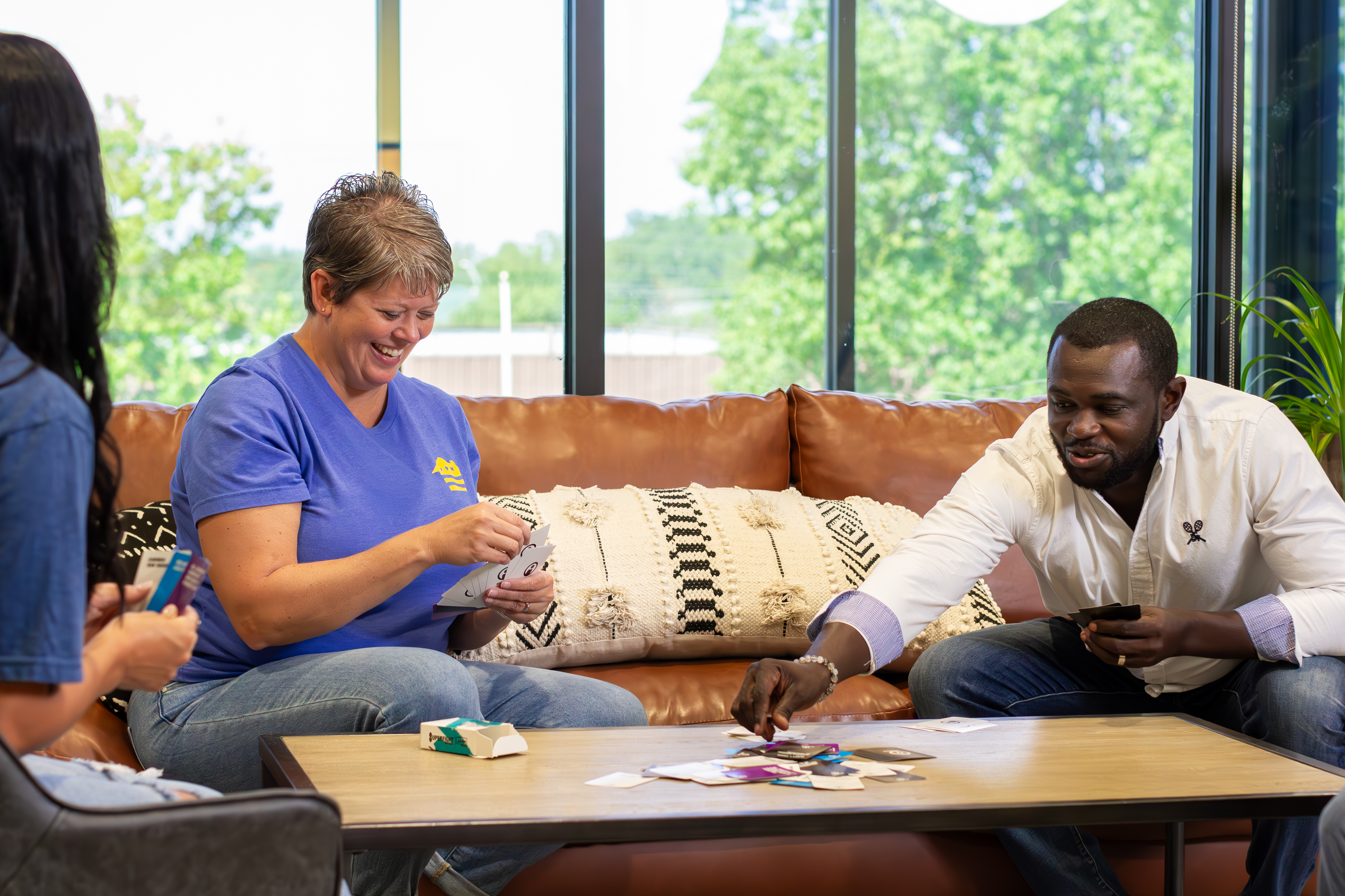 2 female and 1 male emoployee smiling and playing a board game in a glass walled conferance room