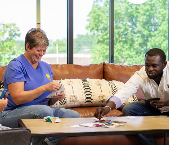 2 female and 1 male emoployee smiling and playing a board game in a glass walled conferance room