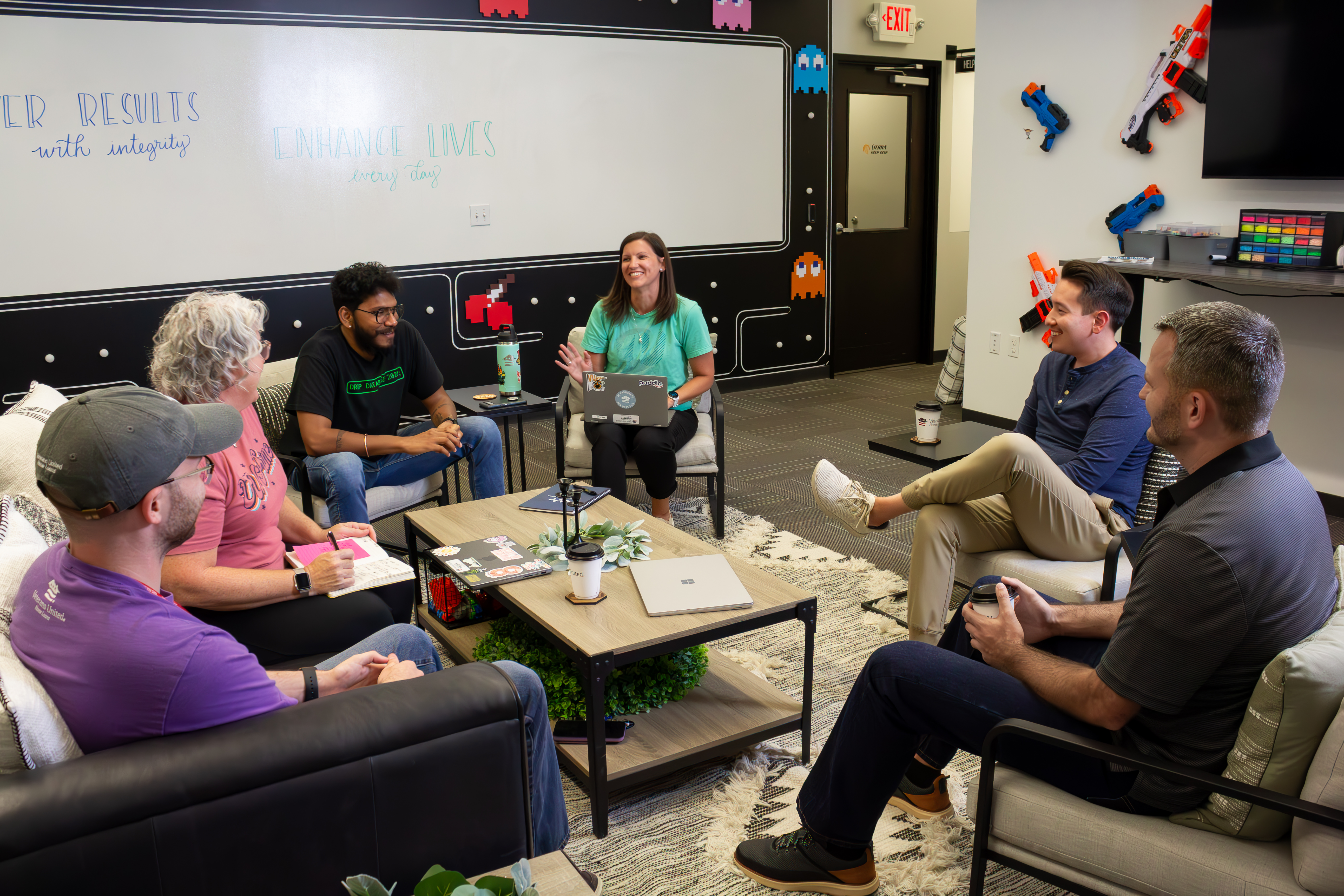 Group of 5 employees in a relaxed meeting on couches and chairs around a coffee table