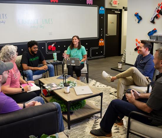 Group of 5 employees in a relaxed meeting on couches and chairs around a coffee table