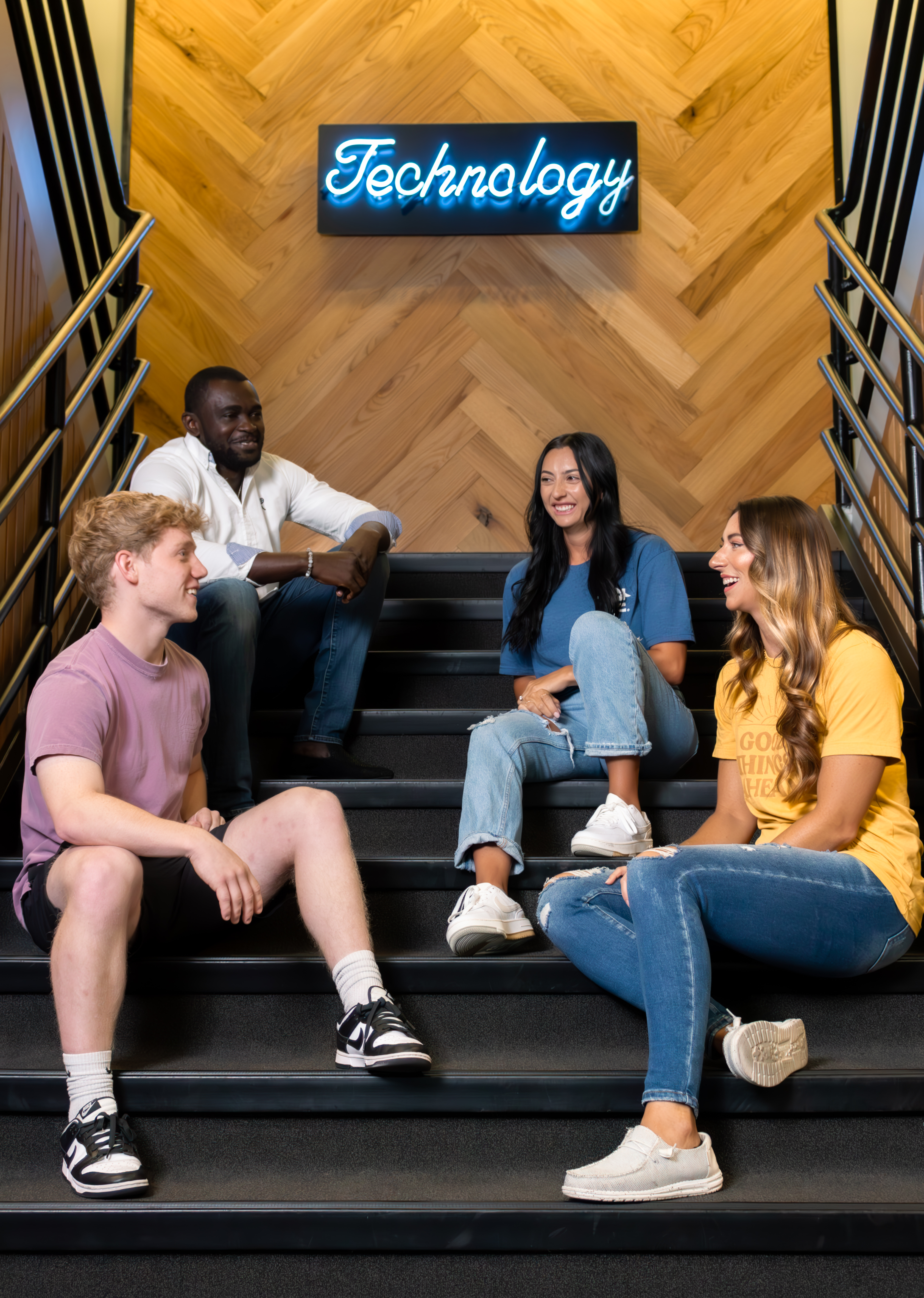 Group sitting on stairs below Technology sign
